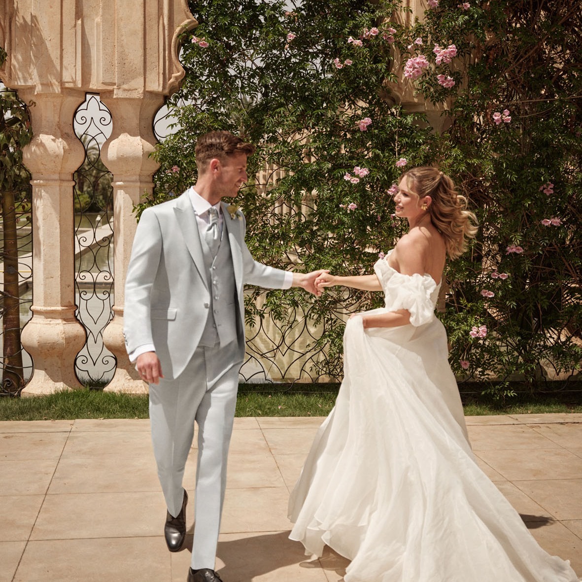 Ein Brautpaar spaziert gemeinsam vor einem wunderschönen Brunnen und strahlt an seinem Hochzeitstag pure Freude aus.