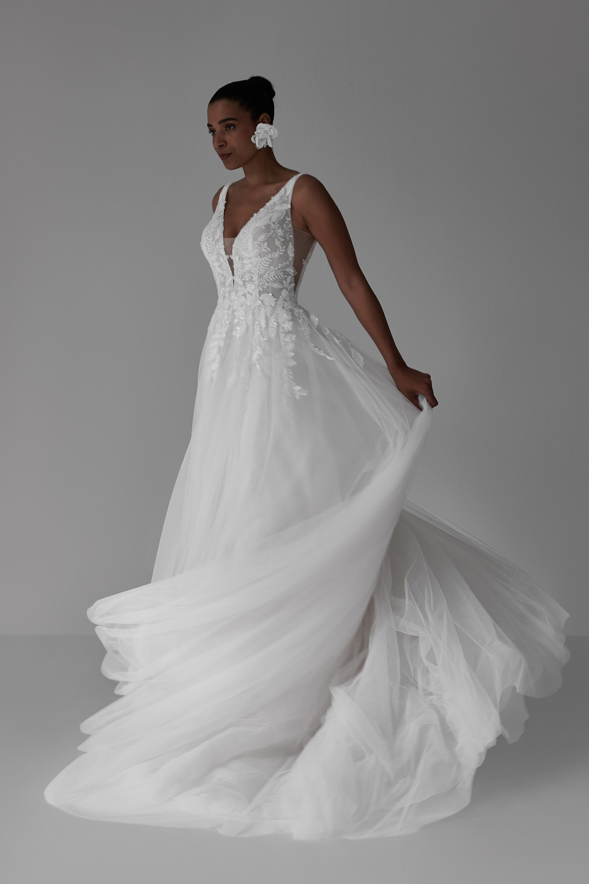 Die Braut in einem weißen Hochzeitskleid mit tiefem V-Ausschnitt steht anmutig da und präsentiert ihren eleganten Stil.