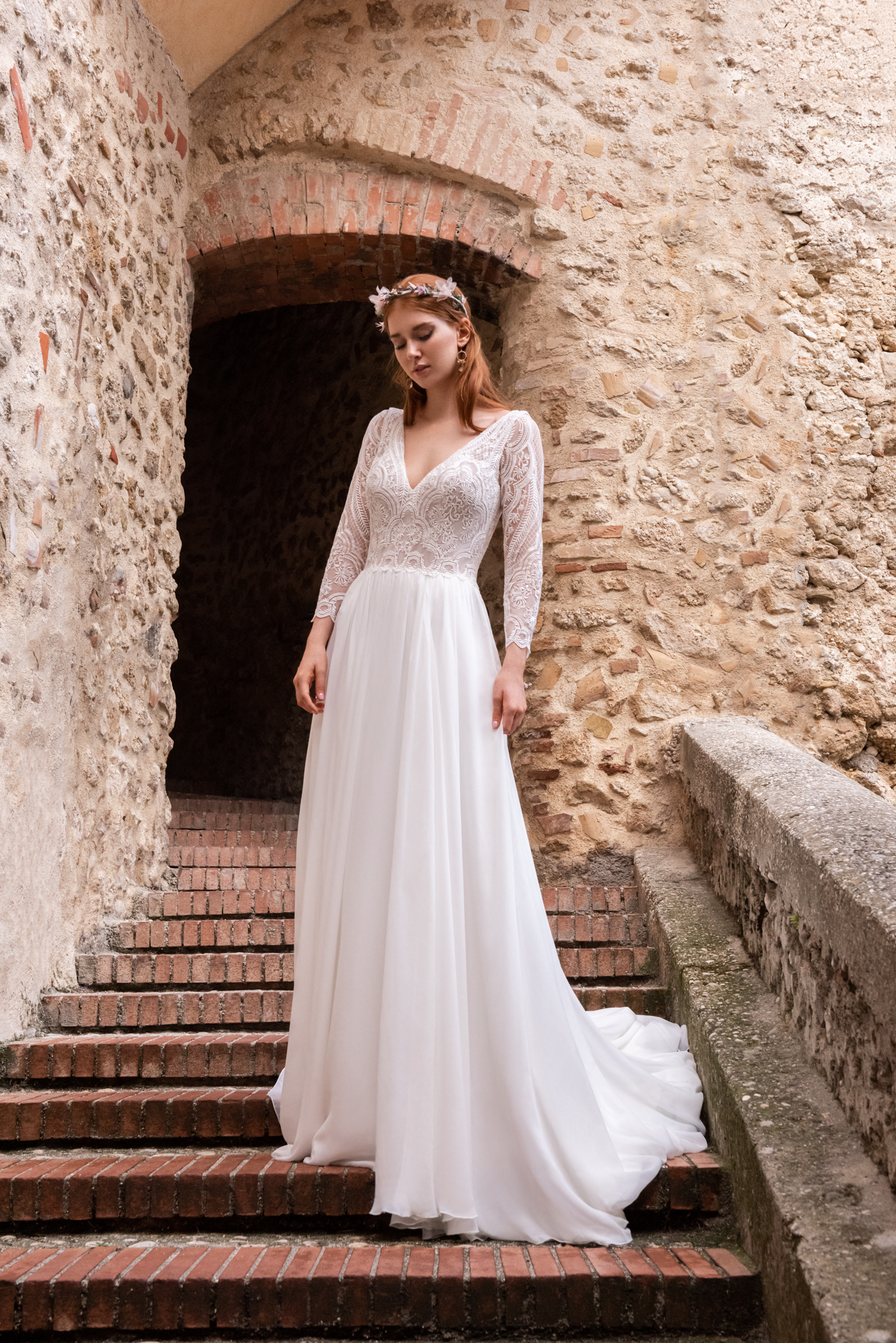 Eine Braut in einem wunderschönen Hochzeitskleid steht anmutig auf einer Treppe und strahlt Freude und Eleganz aus.