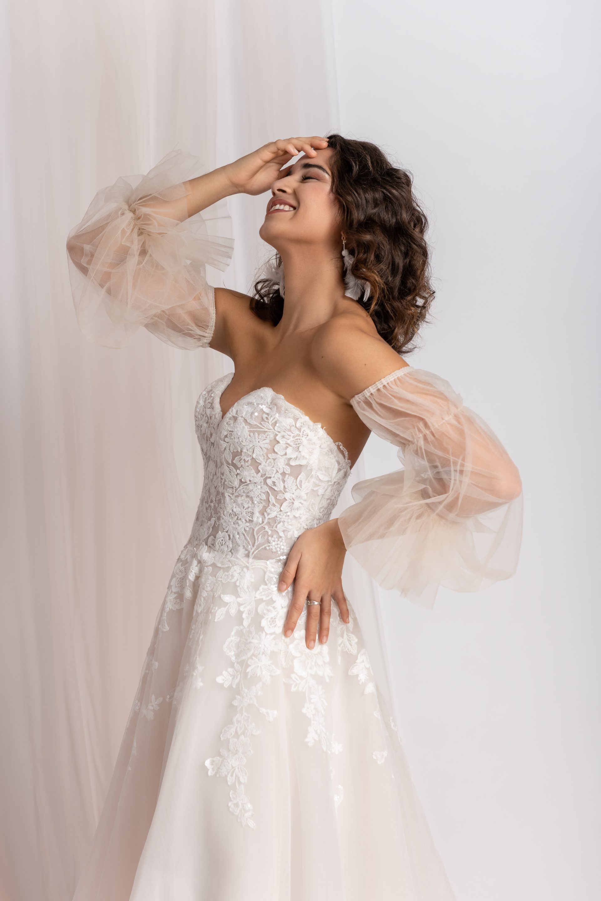 Eine Frau in einem atemberaubenden Brautkleid posiert anmutig für die Kamera und präsentiert ihren freudigen Gesichtsausdruck und ihre elegante Kleidung.