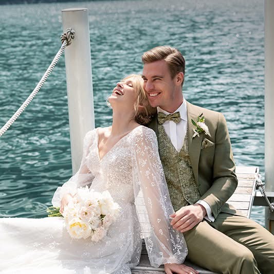 Ein Brautpaar sitzt auf einem Steg und blickt auf einen friedlichen See, umgeben von der Schönheit der Natur.